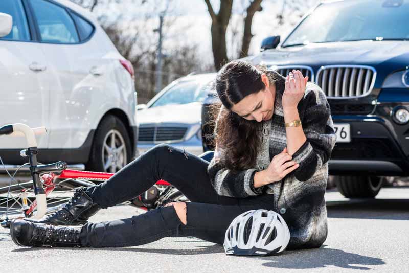 young injured woman, sitting on the ground. bicycle accident next to parked cars on a busy street