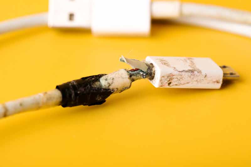 Broken micro USB phone charging cable. Damaged white usb cable plug bandaged by duct tape